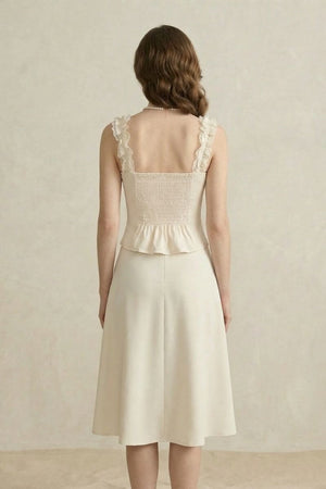 Back view of a model in an ivory corset top with smocked back and lace straps paired with an ivory A-line midi skirt.