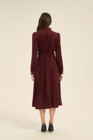 Rear view of a model wearing a long-sleeve burgundy midi dress with a belted waist and collared neckline, styled with black lace heels.