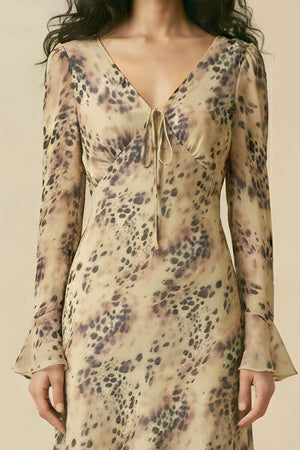 A close-up view of a woman wearing a beige animal-print chiffon midi dress featuring a V-neckline, tie-front detail, and long flared sleeves.