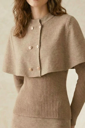 Close-up of the beige knit dress showing the structured cape overlay, textured fabric, and decorative gold-tone double-breasted buttons over a ribbed fitted bodice.