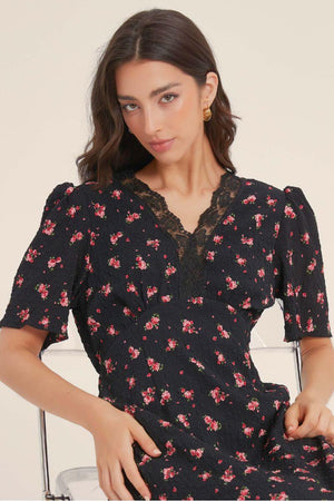 Close-up of a black floral dress featuring a scalloped lace V-neckline and puff sleeves, showing fine texture and intricate floral embroidery.
