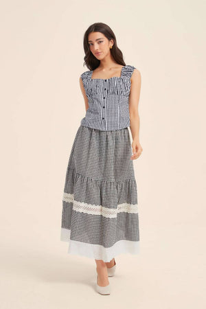 Woman wearing a black gingham ruched-strap top and matching lace-trim tiered skirt, styled with gold earrings and white flats for a classic vintage mood.