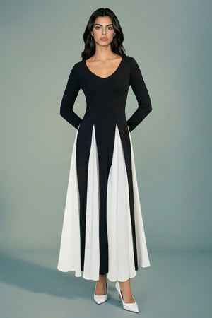 A model faces the camera in a black long-sleeve maxi dress with a plunging neckline and softly flared ivory panels, creating a refined and sculpted look.