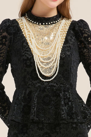 Close-up of a black lace peplum dress featuring gold sequin paneling and layered pearl embellishments around the neckline, highlighting its luxurious texture.