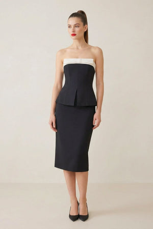 Full-body view of a model in a black strapless peplum top with a white neckline and a black pencil-style midi skirt.