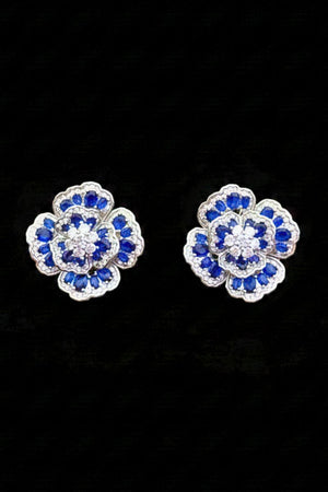 Pair of blue floral gemstone stud earrings displayed on a black background, highlighting the layered flower design and contrasting blue and clear stones.
