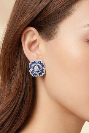 Side profile of a model wearing blue flower-shaped gemstone stud earrings with a silver-tone setting and multi-layered petal details.
