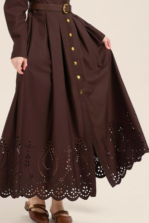 Detailed close-up of brown cotton fabric with floral eyelet embroidery and scalloped hem, showing craftsmanship and texture.