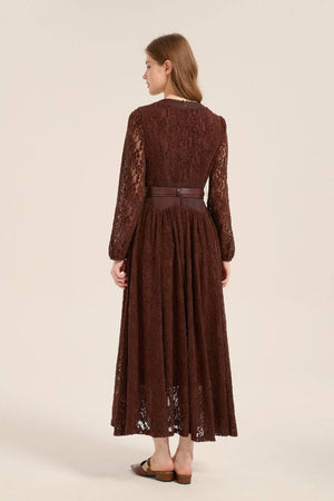 Model showing the back of a brown lace long sleeve maxi dress with a belted waist and full lace overlay, styled with brown flats.