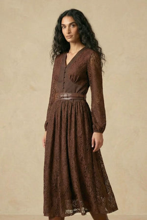 A woman in a brown lace long-sleeve midi dress with a V-neck structured bodice, decorative buttons, and a wide leather waist belt, shown from an angled front pose.