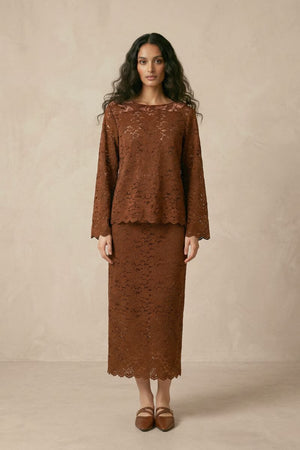 A woman wearing a brown lace long-sleeve top paired with a matching lace midi skirt, both featuring scalloped hems and floral lace detailing.