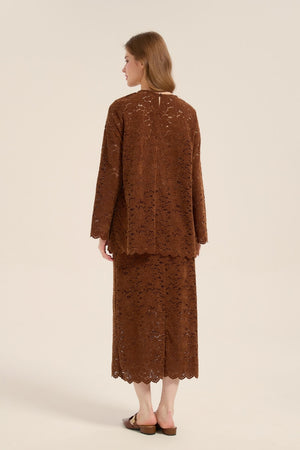 Model wearing a brown lace two-piece outfit from behind, featuring long-sleeve top and midi skirt with scalloped edges and relaxed silhouette.