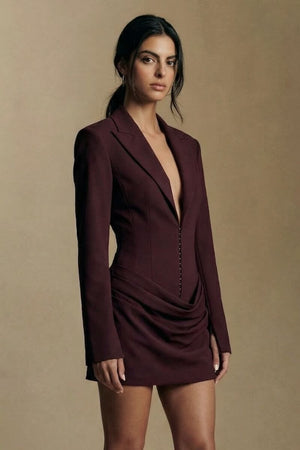 Model shown in a close front view wearing a burgundy blazer mini dress, highlighting the structured lapels, deep V neckline, and softly draped skirt detail.