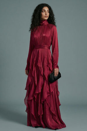 A model in a burgundy high-neck maxi dress is shown in a three-quarter pose, highlighting the fluid drape, gathered waist, and dimensional ruffle detailing.