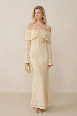 Model in a buttercream lace off-shoulder maxi dress shown from a slight angle, highlighting the delicate lace texture, structured waist, and elegant floor-length cut.
