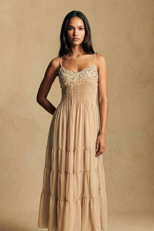 A straight-on studio shot of a model wearing a champagne embroidered bodice maxi dress with a fluid tiered silhouette and delicate pleating, conveying an effortless romantic mood.