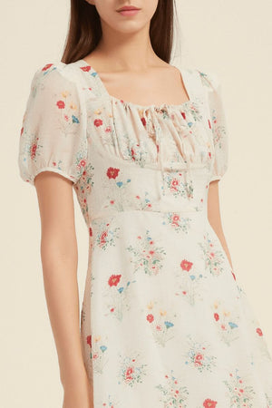 Detailed close-up of a cream floral midi dress highlighting ruched neckline, delicate puff sleeves, and lightweight chiffon fabric texture.