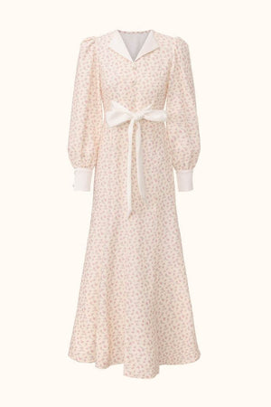 Front view of a cream midi dress with pink floral print, puff sleeves, white cuffs and collar, and a statement waist bow.