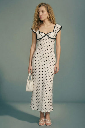 Side view of the cream polka dot lace trim midi dress showing the fitted waist, soft drape, and flutter sleeves, styled with white heels.
