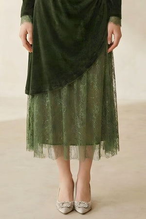 A close-up of the lower half of a dark green velvet and lace midi dress, highlighting the sheer embroidered lace hem and delicate drape.