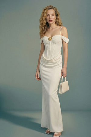 Model in an off-shoulder ivory corset maxi dress showing the smooth draped satin skirt and fitted waist, paired with minimal heels and a structured ivory handbag.
