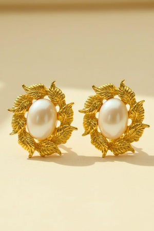 A pair of gold leaf–inspired stud earrings featuring luminous oval pearls, styled symmetrically on a soft neutral surface in a classic Sioéne aesthetic.