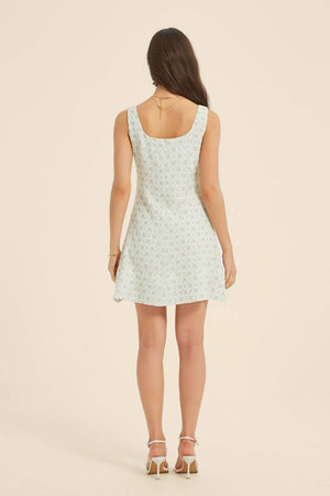 Back view of a woman in a green jacquard floral mini dress with a scoop neckline and A-line silhouette, styled with gold accessories.