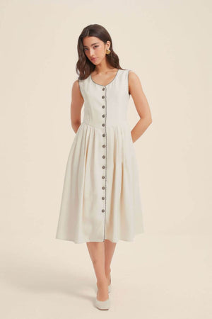 Front view of a sleeveless ivory midi dress with contrast piping and vintage-style buttons down the front, featuring a fitted bodice and softly pleated skirt.
