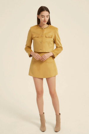 Model in a mustard yellow two-piece mini dress set with a beaded round neckline, gold button details, and structured cropped jacket — vintage elegance meets modern chic.
