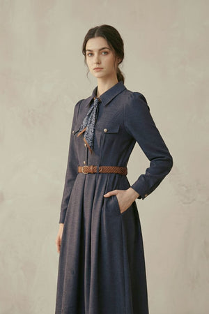A woman in a navy collared midi dress featuring long sleeves, gold-tone buttons, a printed neck scarf, and a brown braided belt, shown from an angled front pose.
