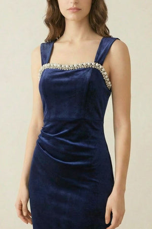 A close-up of a navy velvet gown showing the pearl-trimmed square neckline and the smooth fitted bodice in soft lighting.