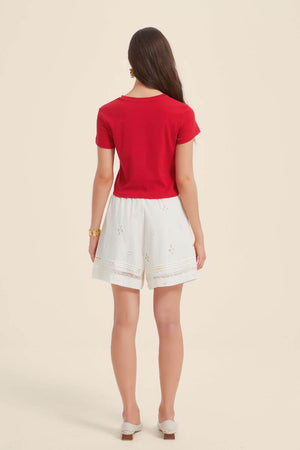 Back view of a red short-sleeve cropped T-shirt and white embroidered shorts featuring delicate cut-out details and lace-trimmed hem.
