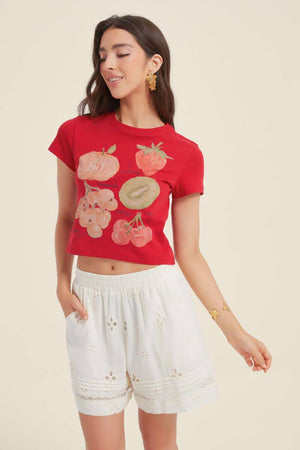 Model in a red cropped T-shirt with watercolor fruit illustrations, paired with white lace-trim shorts — a relaxed and cheerful Sioéne daytime outfit.