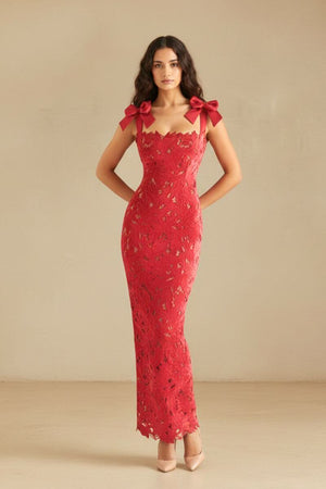 Model posing in a red lace bow-shoulder gown with a body-skimming fit and floral cutouts, hands placed behind her back.