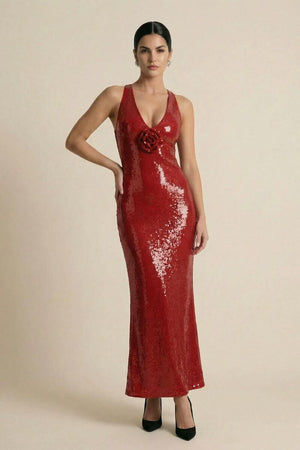 Full-length front view of a model wearing a shimmering red sequin halter maxi dress with a plunging neckline and rose detail at the chest, styled with black stilettos on a clean studio backdrop.