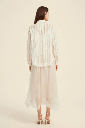 Back view of a model wearing a sheer cream lace button-up blouse paired with a soft layered tulle midi skirt.