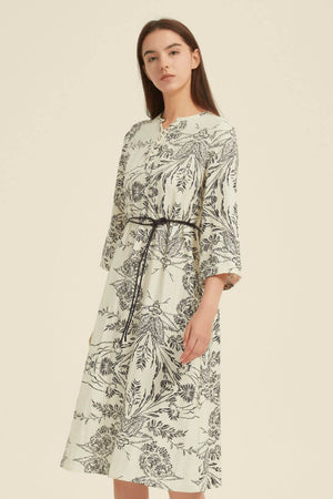 Side profile of a cream midi dress showcasing black botanical motifs, a notch neckline, and 3/4 sleeves with a cinched waist.