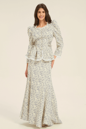 Model smiling while wearing a cream and blue floral peplum blouse with puff sleeves and matching maxi skirt, front view.