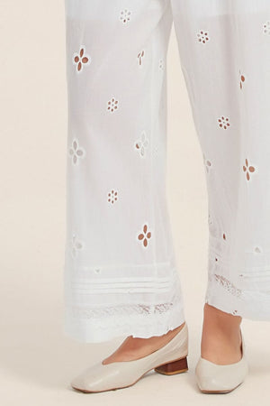 Close-up of white wide-leg pants featuring floral eyelet embroidery and scalloped lace hem, styled with beige low-heel flats.
