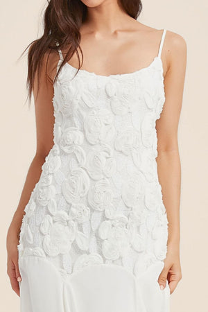 Close-up of a white floral appliqué maxi dress featuring three-dimensional rosette embroidery and delicate lace texture on the bodice.