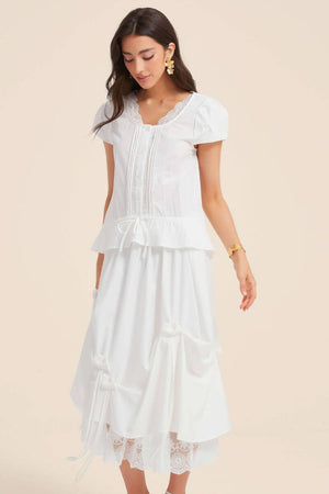 Woman wearing a white lace-trim pintuck blouse with matching bow-draped skirt, creating a romantic monochrome outfit with lace hem detailing.