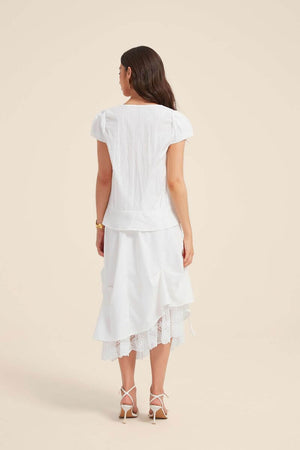 Back view of a woman wearing a white lace-trim blouse and bow-draped skirt set, highlighting the tiered structure and lace-edged hemline.