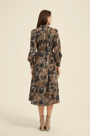 Back view of a vintage-inspired midi dress featuring an intricate floral and geometric print in earthy tones, long puff sleeves, a high neckline, and a belted waist for a flattering silhouette.