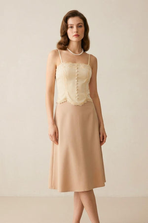 Full-body view of a model in an ivory lace corset top and flowy beige midi skirt, standing gracefully in a neutral-toned studio.