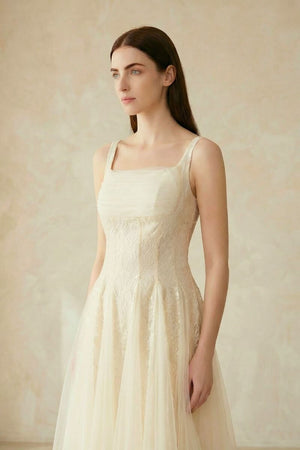 A woman wearing an ivory lace tulle midi dress, shown from a soft side angle highlighting the fitted bodice and flowing skirt.