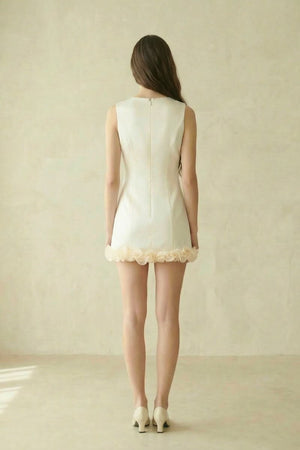 back view of an ivory sleeveless mini dress with concealed zipper and rosette hem, shown in a soft neutral studio setting.