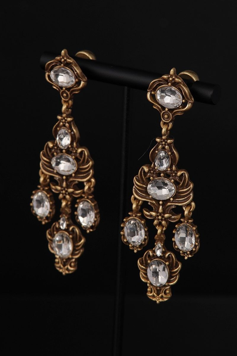 Side angle view of antique gold chandelier earrings with clear crystals highlighting dimensional metalwork and dangling silhouette.