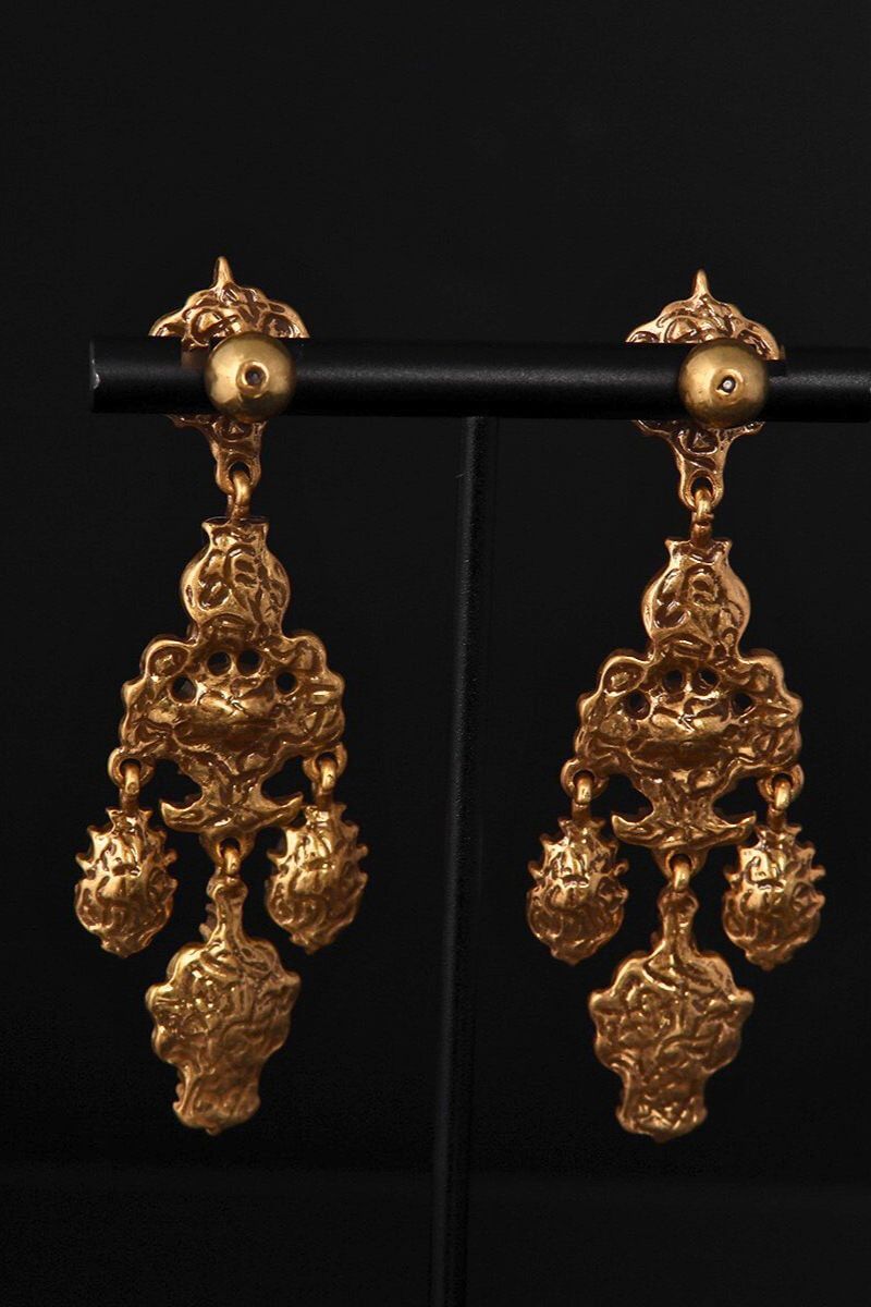 Back view of antique gold chandelier earrings showing sculpted metal backing and drop structure on a black jewelry stand.