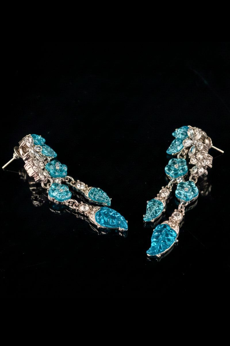 A close angled view of aqua blue crystal leaf drop earrings, showing the dimensional setting, faceted stones, and delicate dangling construction.