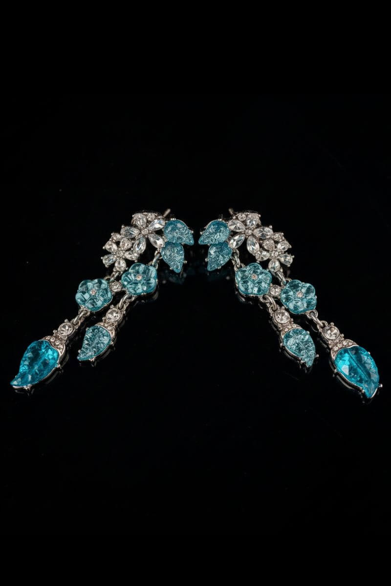 Aqua blue crystal leaf drop earrings displayed in a soft curved layout on a black background, highlighting the layered crystal and silver-tone setting.